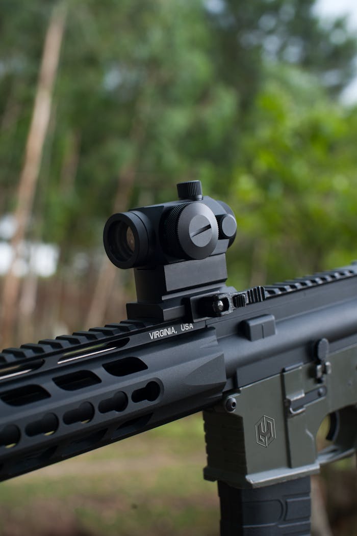 Close-up image of a rifle with a precision scope, shot outdoors with a blurred background.